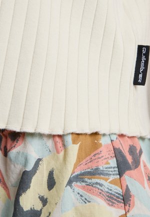 Close-up van geribd crèmekleurig stof met een zwart Quiksilver-label boven meerkleurig bloemmotiefstof in zachte pasteltinten.