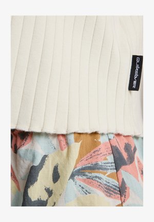 Nahaufnahme von geripptem cremefarbenem Stoff mit schwarzem Quiksilver-Label über mehrfarbigem, floral gemustertem Stoff in weichen Pastelltönen.