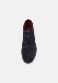 Botín de ante azul marino con forro de tela roja, punta redonda y cordones texturizados en contraste. Suela de goma plana. Diseño simple.