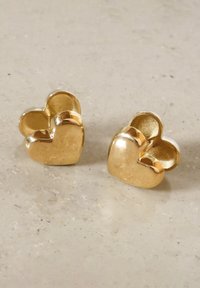 Goldene, herzförmige Ohrringe mit glänzender Oberfläche und erhabenem Design. Zwei ineinander verschlungene Herzen erzeugen einen tridimensionalen Effekt.