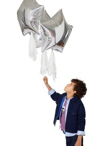 Drie zilveren stervormige ballonnen met witte linten worden vastgehouden door een kind dat een marineblauwe jas over een paarse shirt draagt en omhoog kijkt.