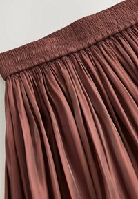 Jupe plissée marron avec une large ceinture élastique froncée, en tissu lisse et brillant.