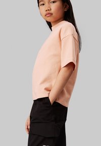 Lichtroze t-shirt met korte mouwen van zachte katoen, met een ontspannen pasvorm en een ronde halslijn, gestyled met zwarte cargobroeken.