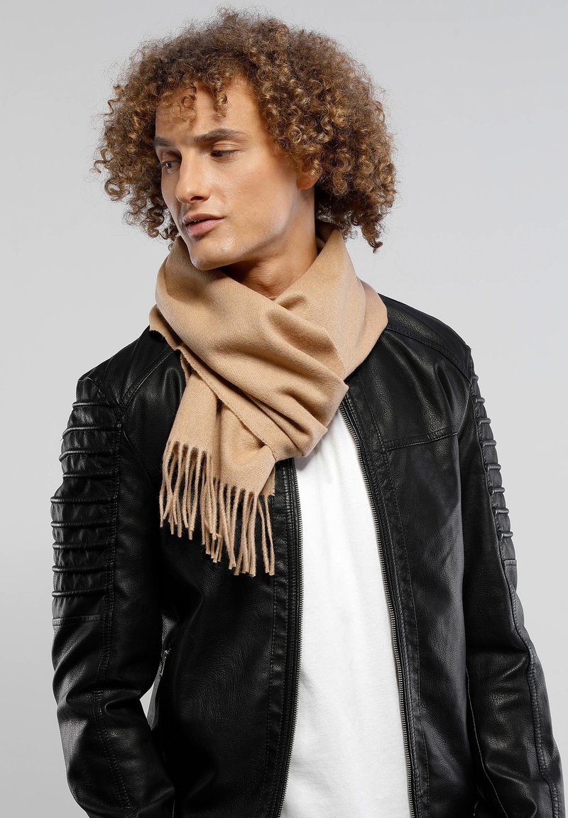 Beige scarf made of soft fabric, featuring fringed ends, worn over a black leather jacket with quilted shoulder details.