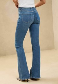 Modri razširjeni kavbojke s srednjim pasom, izdelane iz denima. Imajo klasičen pet-pocket dizajn in subtilno zbledelo obdelavo, v kombinaciji z ostrimi petami.