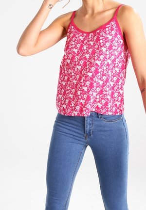 Camisola floral rosa con tirantes finos, de corte suelto, con un estampado de flores blancas. Combinada con pantalones vaqueros ajustados azules.