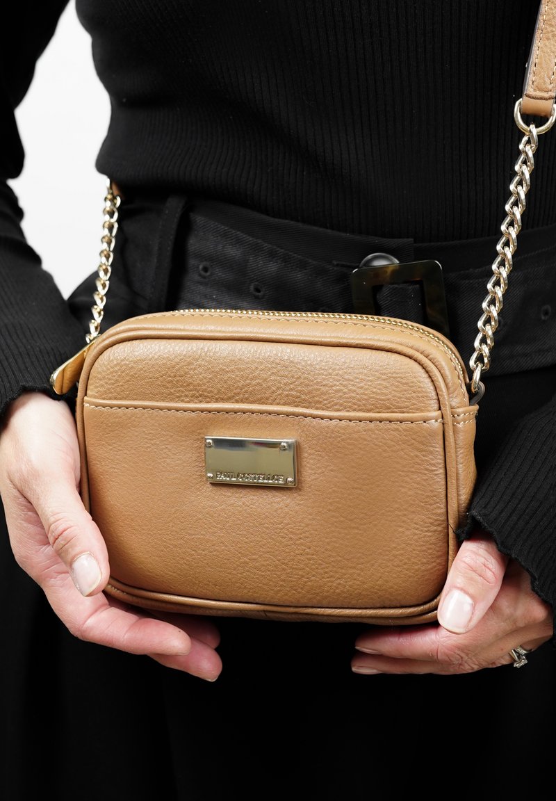 Sac bandoulière en cuir tan avec fermeture éclair, bandoulière en chaîne et plaque métallique. Surface texturée, forme rectangulaire et design épuré.