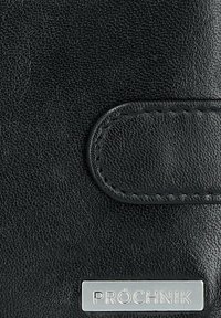 Czarny portfel ze strukturalnej skóry z zapięciem magnetycznym, z metalową blaszką z logo z wytłoczonym napisem "PRÓCHNIK". Gładka powierzchnia z detalami w postaci przeszyć.