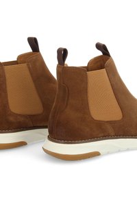 Bottines en cuir suédé marron avec panneaux latéraux élastiques, languette assortie et semelle en caoutchouc blanche. Détails cousus le long du bord.