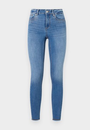 Skinny jeans made of light blue denim, featuring decorative studs on the front pocket area and a frayed hem at the ankle.