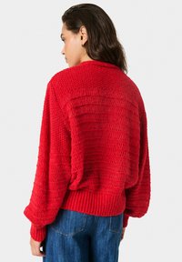 Pulover roșu tricotat, cu o croială liberă, având un design texturat, cu țesătură deschisă, manșete cu model în rib și un decolteu larg.