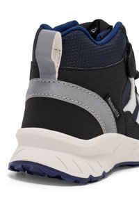 Svart och marinblå hög sneakers som har en texturerad yta, grå detaljer, vit mellansula och ett mönstrat gummisul.