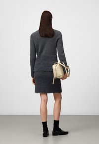 Grijze gebreide trui met ribbelstructuur, voorzien van een fuzzy zoom, gecombineerd met een bijpassende rok. Een lichtbeige tas maakt de outfit compleet.
