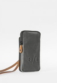 Compact black leather wallet with a zip closure, featuring a tan strap and embossed lettering on the front. Minimalistic and rectangular design.