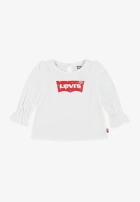 Fehér, hosszú ujjú póló fodros mandzsettával, elől piros Levi's logóval. Puha pamut anyag, kerek nyakkivágás, kulcslyukas hátsó záródás.