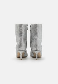 Botas de tobillo plateadas hechas de material texturizado, con un diseño ajustado, punta afilada y tacones altos y delgados. Cremallera en el interior.