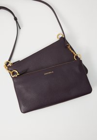 Borsa a tracolla in pelle viola scuro con dettagli in oro, dotata di due scomparti con zip e una tracolla regolabile. Dettagli in superficie testurizzata visibili.