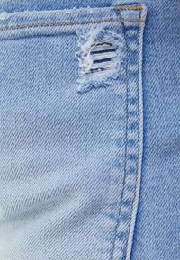 Ljusblå denimtyg med en fransig reva och horisontella skåror. Synliga sömmar längs kanten ger detalj till designen.