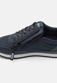Sneaker blu scuro con upper testurizzato, dotato di lacci, cerniera laterale e una suola intermedia bianca con suola esterna in gomma nera.