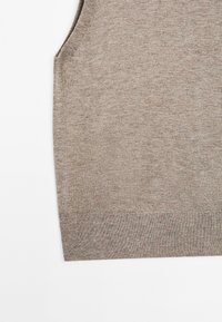 Beige ilmanhihaisesti neulepaita, jossa on sileä tekstuuri, pyöreä pääntie ja hillitty heather-kuvio. Reunat on viimeistelty yksinkertaisella helmalla.