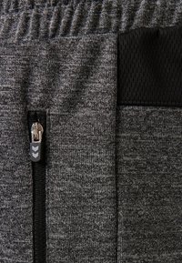 Graue Sporthose aus strukturiertem Stoff mit elastischem Bund, Reißverschlusstasche und schwarzem Mesh-Akzent an der Seite.