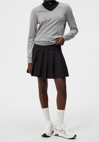 Grå V-ringad sweater över en svart veckad kjol, kombinerat med vita sneakers och sportstrumpor; slät tygkvalitet med en minimalistisk design.