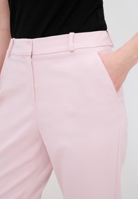Lichtroze broeken van glad materiaal hebben een op maat gemaakte uitstraling met een ritssluiting, riemlussen en zijzakken.