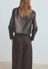 Ciemnobrązowa skórzana krótka kurtka z szerokimi rękawami, zestawiona z wysokim stanem ciemnobrązowych spodni. Gładka tekstura, minimalistyczny design.