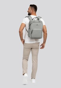 Zaino grigio con scomparti multipli, spallacci imbottiti e un design elegante. Indossato da una persona in abbigliamento casual.