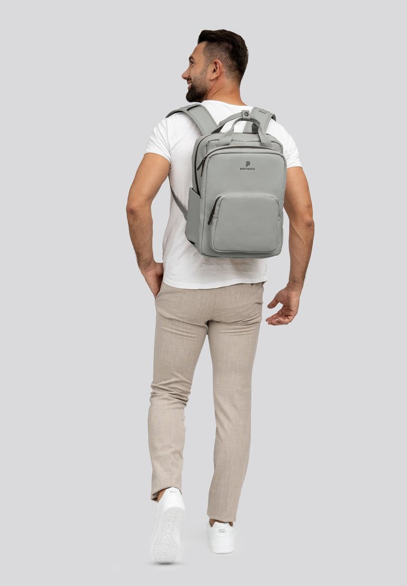 Zaino grigio con scomparti multipli, spallacci imbottiti e un design elegante. Indossato da una persona in abbigliamento casual.