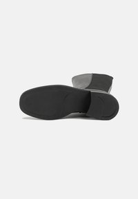 Bota preta até ao tornozelo com um upper texturizado e uma sola lisa. O design inclui um bico arredondado e um salto baixo.