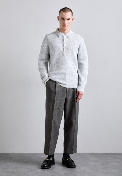 Heledad hall hallide pullover kootud helesinises värvitoonis, millel on krae ja nööbivöö, kombineeritud hallide laia jalgadega pükstega ning mustade nahast mokassiinidega, millel on kuldne riistvara.