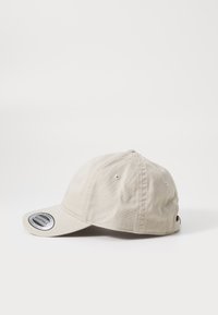 Beige bomull baseball cap med buet skygge, justerbar stropp og ventilhull på toppen. Har en rund etikett foran.