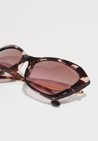 Óculos de sol marrom-tartaruga com lentes gradientes rosa, armação de plástico angular e acentos dourados, apresentando o logótipo "vogue" na lente.