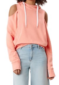 Haut à capuche rose décolleté avec des cordons blancs, en tissu doux et accents côtelés, accompagné de jeans taille haute bleu clair.