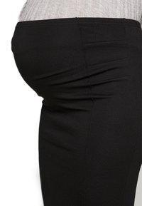 Černé elastické legíny s hladkou texturou, jemnými švy a přiléhavým střihem, které pevně obepínají pas a stehna.