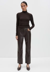 Bruine coltrui gemaakt van zachte stof, gecombineerd met strakke, high-waisted, donkerbruine leren broek met zijzakken en een knoopdetail.
