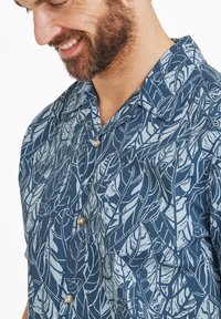 Short-sleeve, button-up shirt in dark blue fabric featuring a light leaf pattern, with a spread collar and brown buttons. Smooth texture.