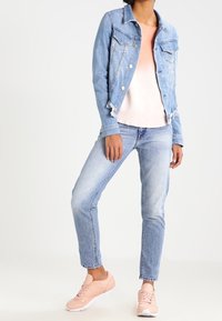 Lichtblauwe spijkerjasje met zakken, gecombineerd met een roze top met verloop en lichtblauwe spijkerbroek. Afgewerkt met roze sneakers.