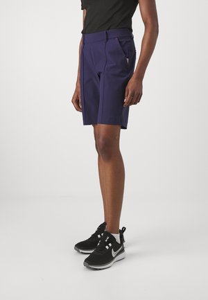 Bermude personalizate de culoare bleumarin, cu un front plat, două buzunare laterale și o textură fină. Asortate cu adidași sport negri.