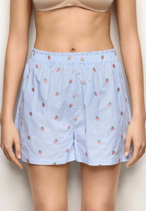 Niebiesko-białe spodenki w paski z małymi różowymi wzorami truskawek, noszone przez osobę z odsłoniętym brzuchem i beżowym topem.