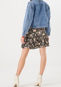 Džínová bunda s dlouhými rukávy, květinová černá sukně s volánky a bílé kotníkové boty s cvočky. Oblečení má městský vrstvený vzhled.