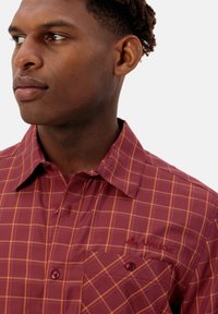 Korte mouwen geruite shirt in bordeauxrood met een oranje ruitpatroon. Voorzien van een knoopsluiting bij de kraag, een borstzak en een gemarkeerd logo aan de voorkant.
