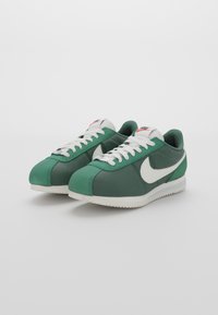 Green textile sneakers with white accents, featuring a textured surface, lace-up design, and a prominent Nike swoosh on the sides.