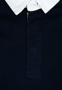 Námořnická modrá polo tričko s bílým límečkem, plaketou na jeden knoflík a texturovanou vazbou, s malým vyšívaným logem nad lemem.