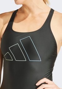 Camiseta sin mangas negra de deporte con una textura suave, que presenta un gran gráfico del logo de Adidas en varios colores en la parte frontal.