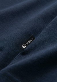 Gros plan sur un tissu bleu marine avec une petite étiquette noire affichant le mot ""ombre"" en blanc, cousue sur le tissu.