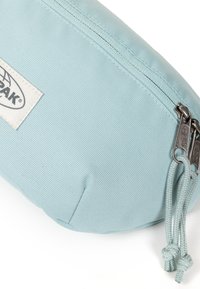 Astuccio azzurro chiaro con zip realizzato in tessuto testurizzato. Presenta un'etichetta con logo intrecciato e tirazip in metallo con accenti in corda intrecciata.