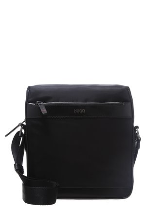 Zwarte schoudertas van glad, synthetisch materiaal. Voorzien van een voorvak met ritssluiting, logodetail en een verstelbare riem.