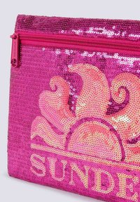 Borsetta con paillettes rosa, caratterizzata da un motivo a sole in pesca e una zip rosa. Il design presenta una superficie liscia e un forte contrasto di colori.